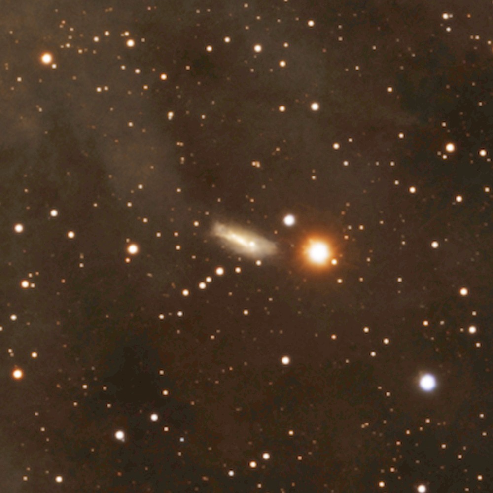 LEDA 3868080 : une galaxie vue par la tranche, à 360 millions d'années-lumière, posée près d'une étoile orange tout au fond du champ.