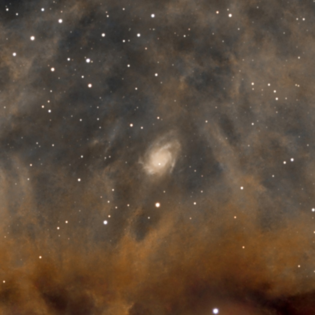 Une lointaine galaxie spirale, à des millions d'années-lumière bien au-delà du nuage, que la longue pose fait surgir en transparence.